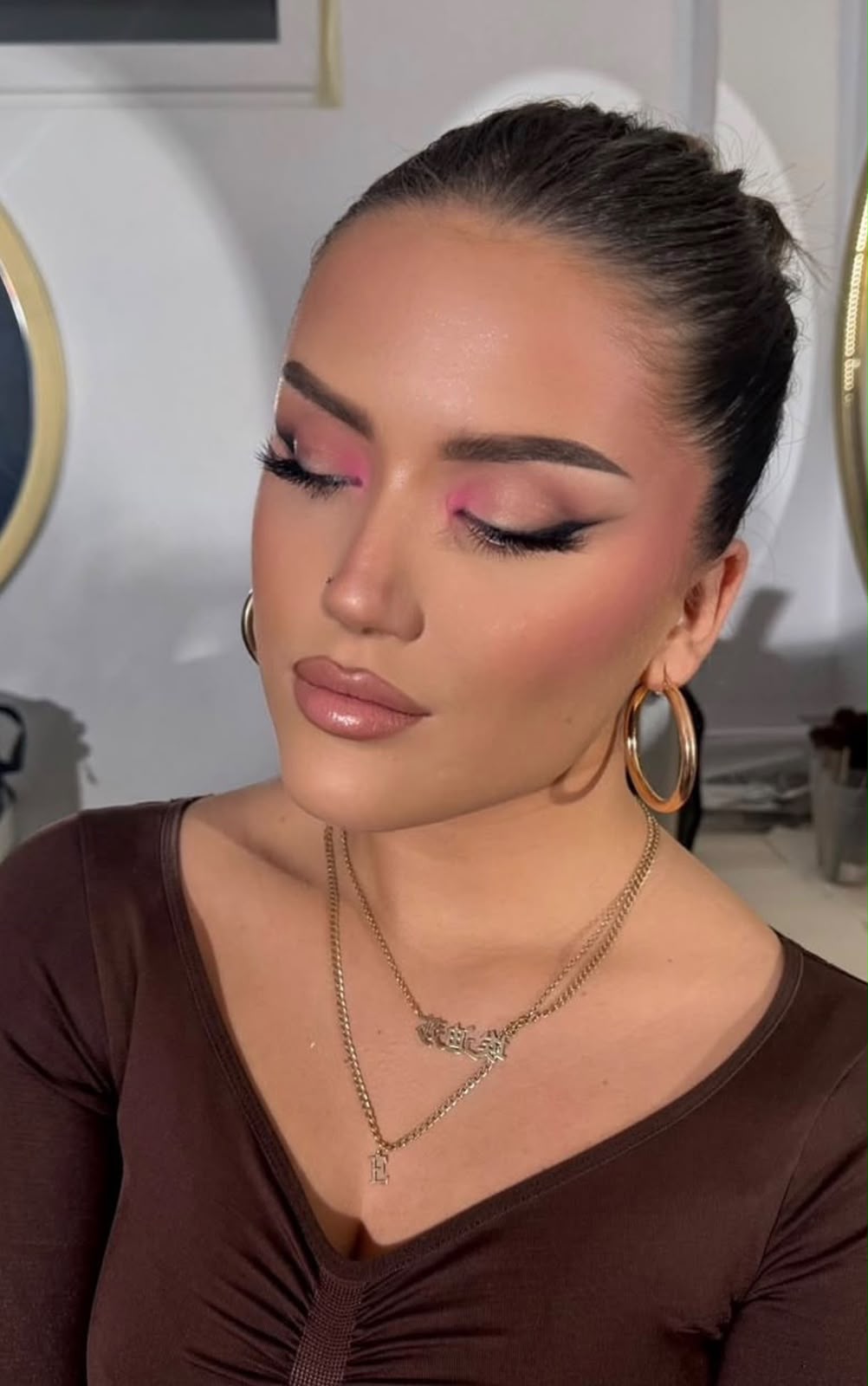 High sleek bun with a pink graphic eye and gold hoops