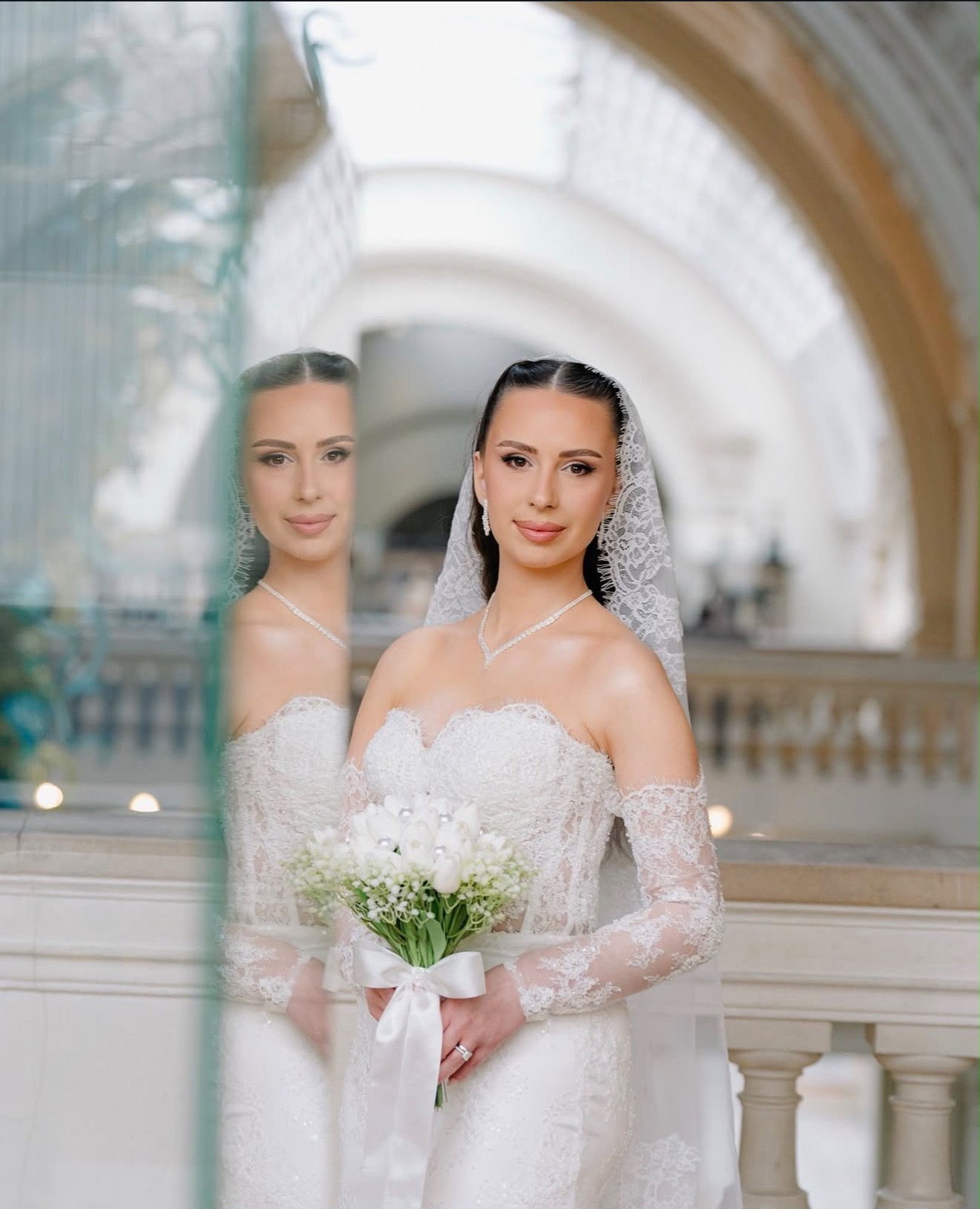 Bride reflected in glass at the venue with veil and bouquet